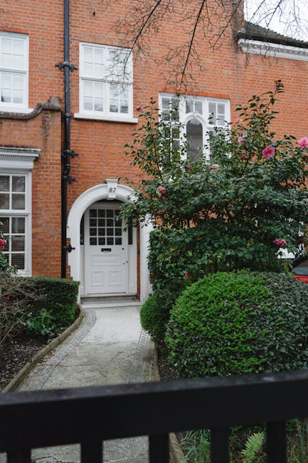 A residential property with a red-brick façade and white-framed windows, featuring an arched doorway with a white door, a letterbox, and a small window above. The entrance is accessed via a curved co